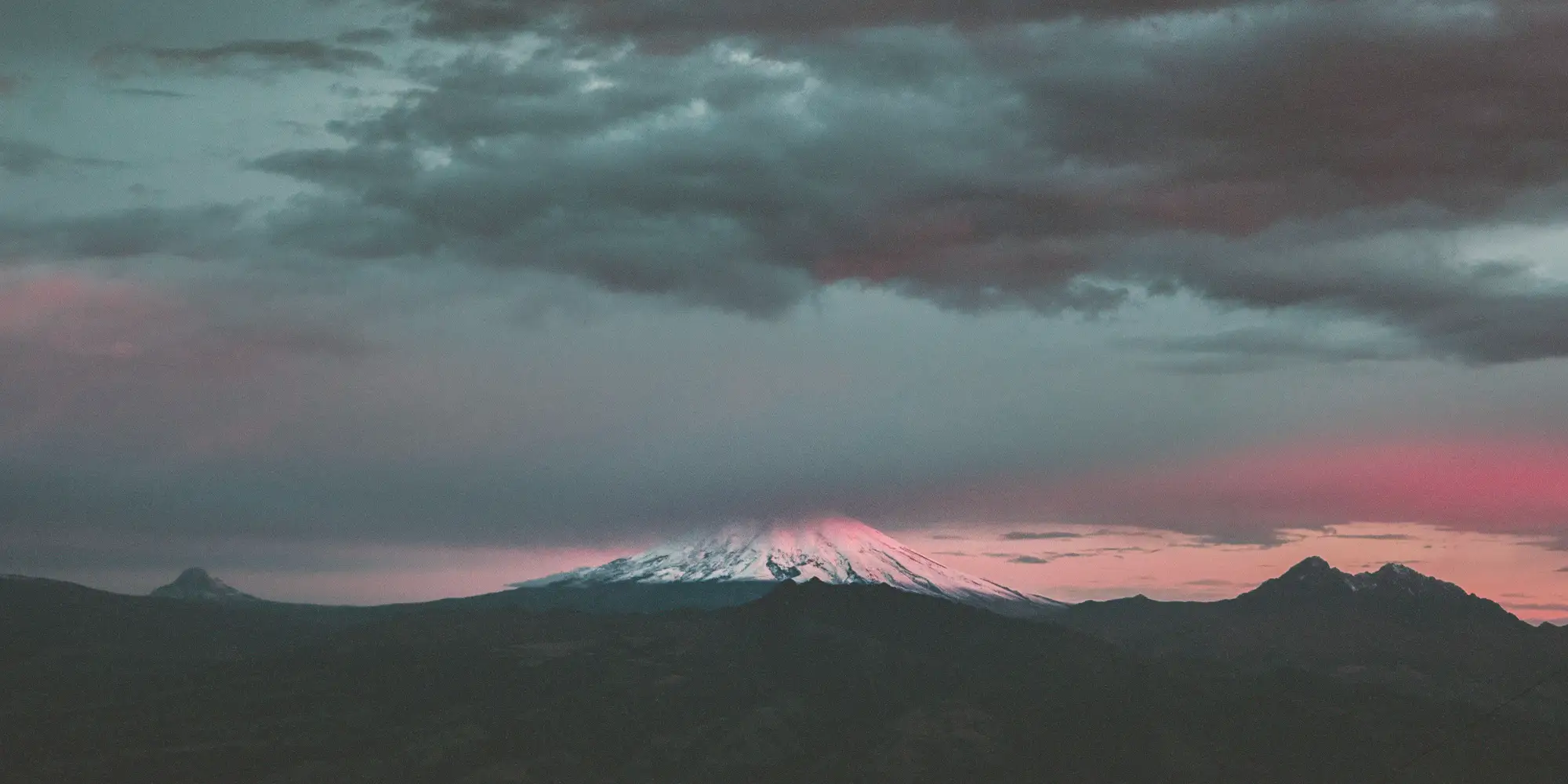 Snow-capped Cotopaxi volcano catching pink dusk light beneath heavy clouds, Ecuador